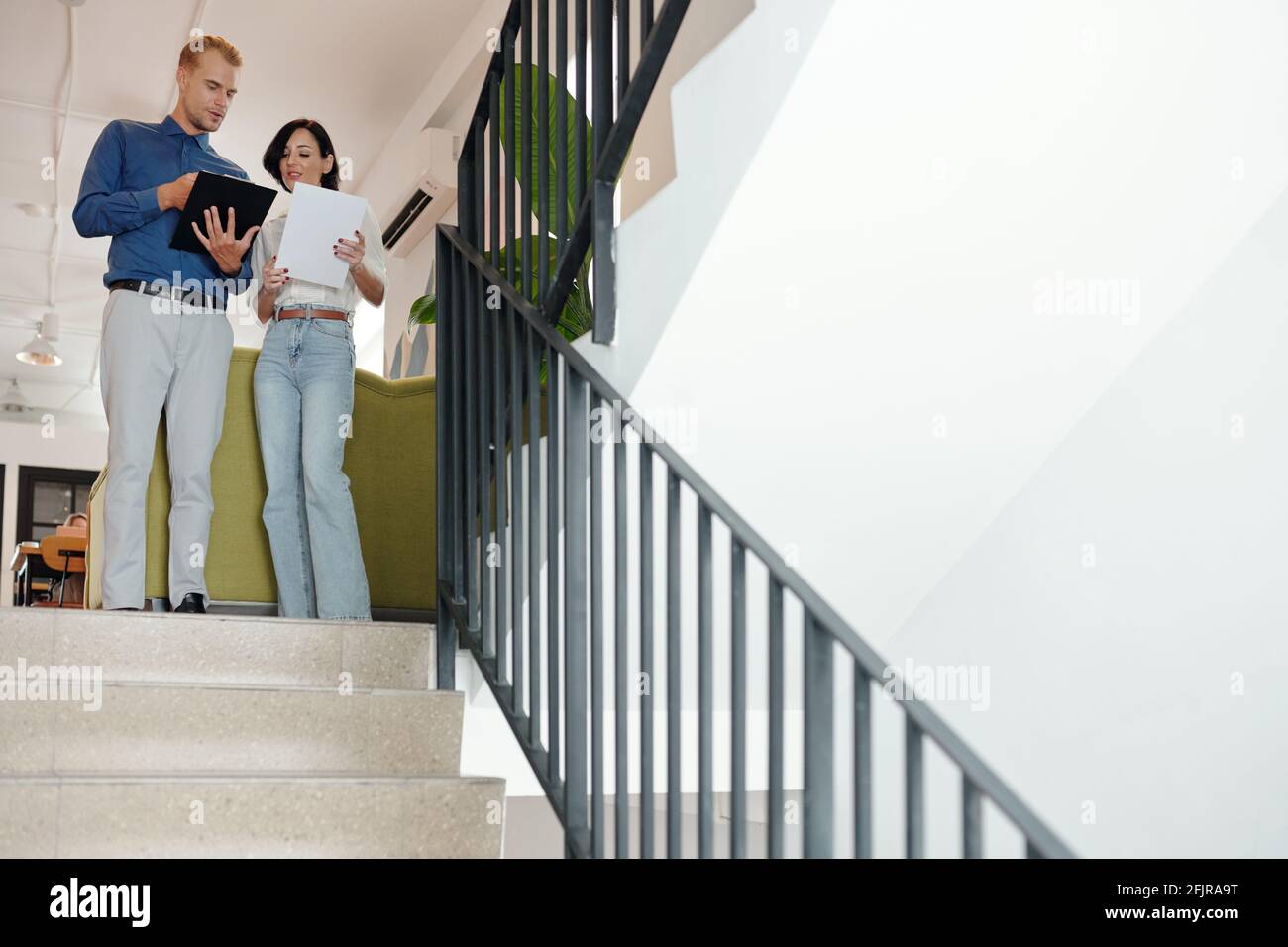 Young entrepreneurs standing on steps and discussing details of project plan Stock Photo