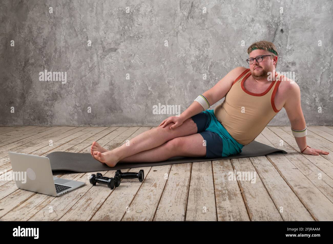funny fat man doing sports on the yoga mat, doing sports online, looking  into the laptop Stock Photo - Alamy