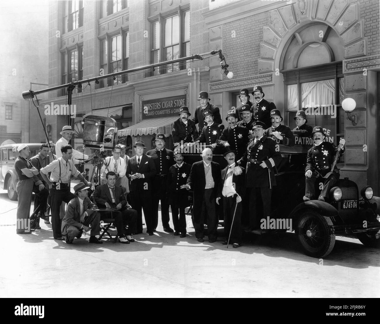 Director RALPH STAUB (seated) CHESTER CONKLIN BEN TURPIN FORD STERLING BOBBY DUNN (on car hood) and other KEYSONE KOPS on set candid with Movie Crew during filming of the slapstick comedy short  KEYSTONE HOTEL 1935 director RALPH STAUB story and screenplay Joe Traub The Vitaphone Corporation / Warner Bros. Stock Photo