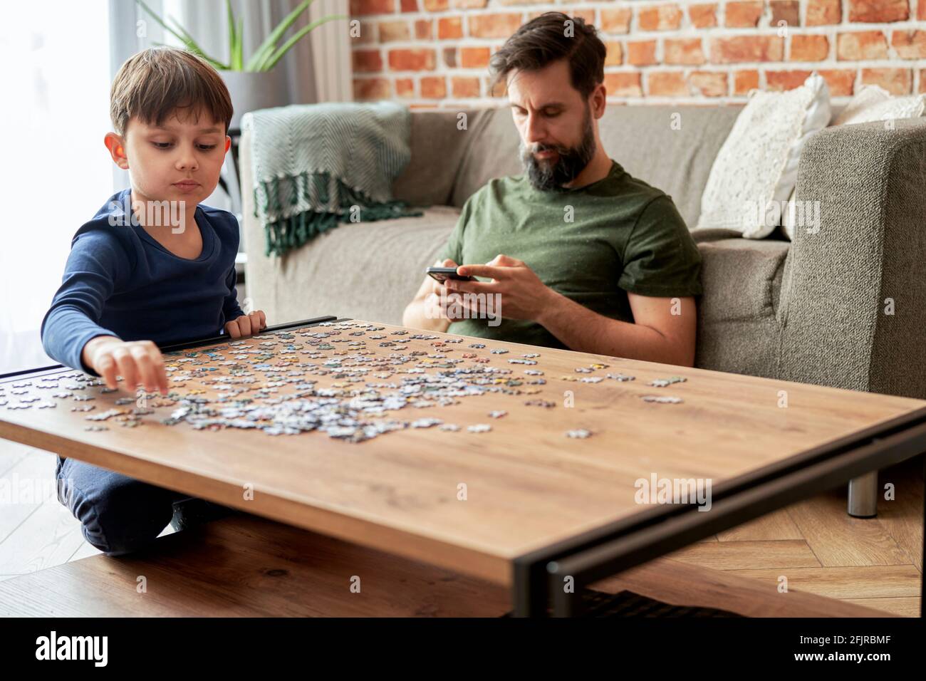 Boy solving jigsaw puzzle during father using Stock Photo