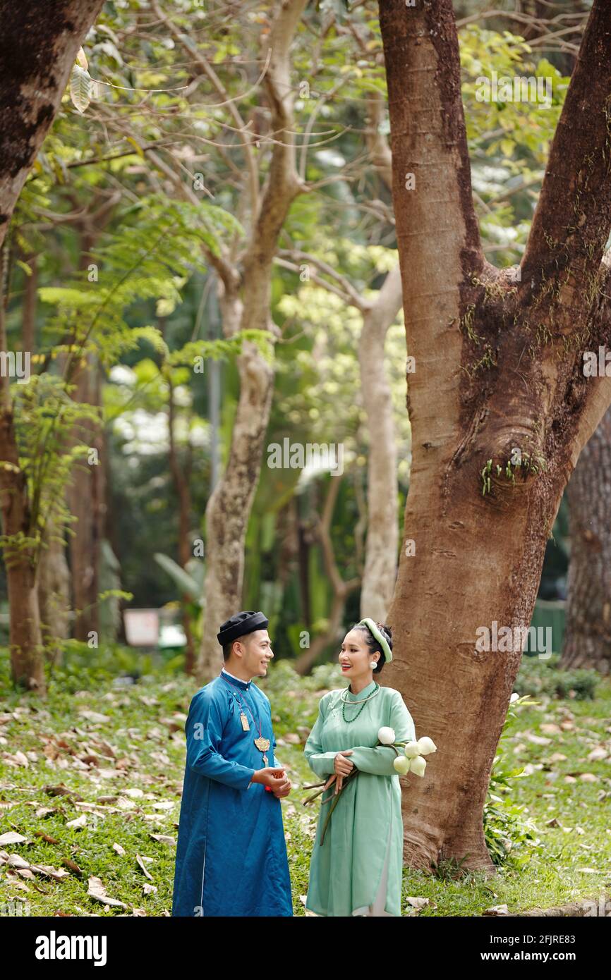 Happy bride and groom in traditional Vietnamese costumes talking in park after having wedding ceremony Stock Photo