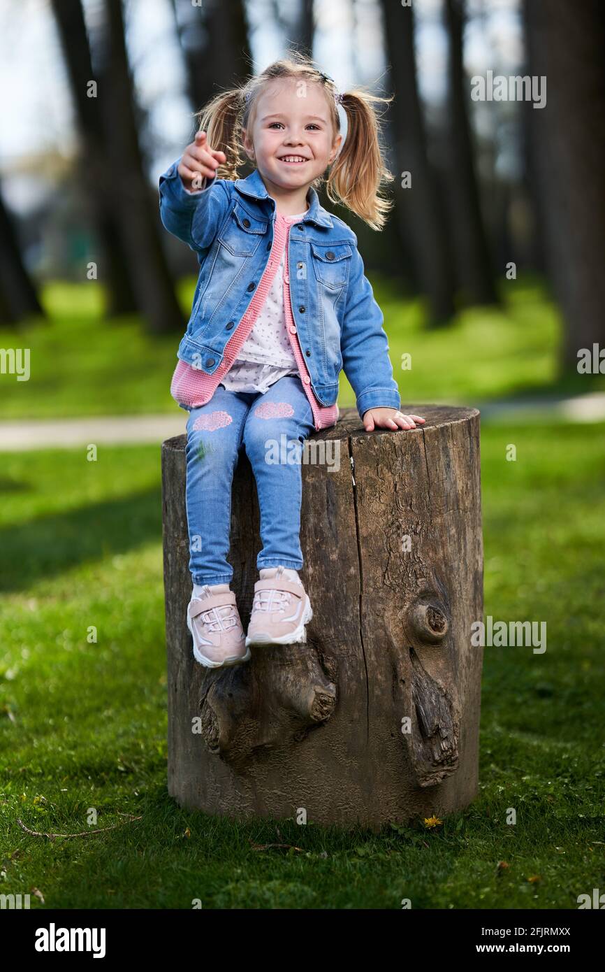 Adorable little girl sitting on a big stump in the park Stock Photo - Alamy