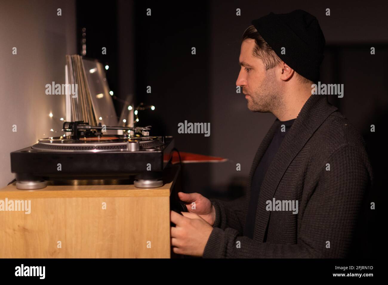 unshaven handsome millennial guy puts record on turntable and taking