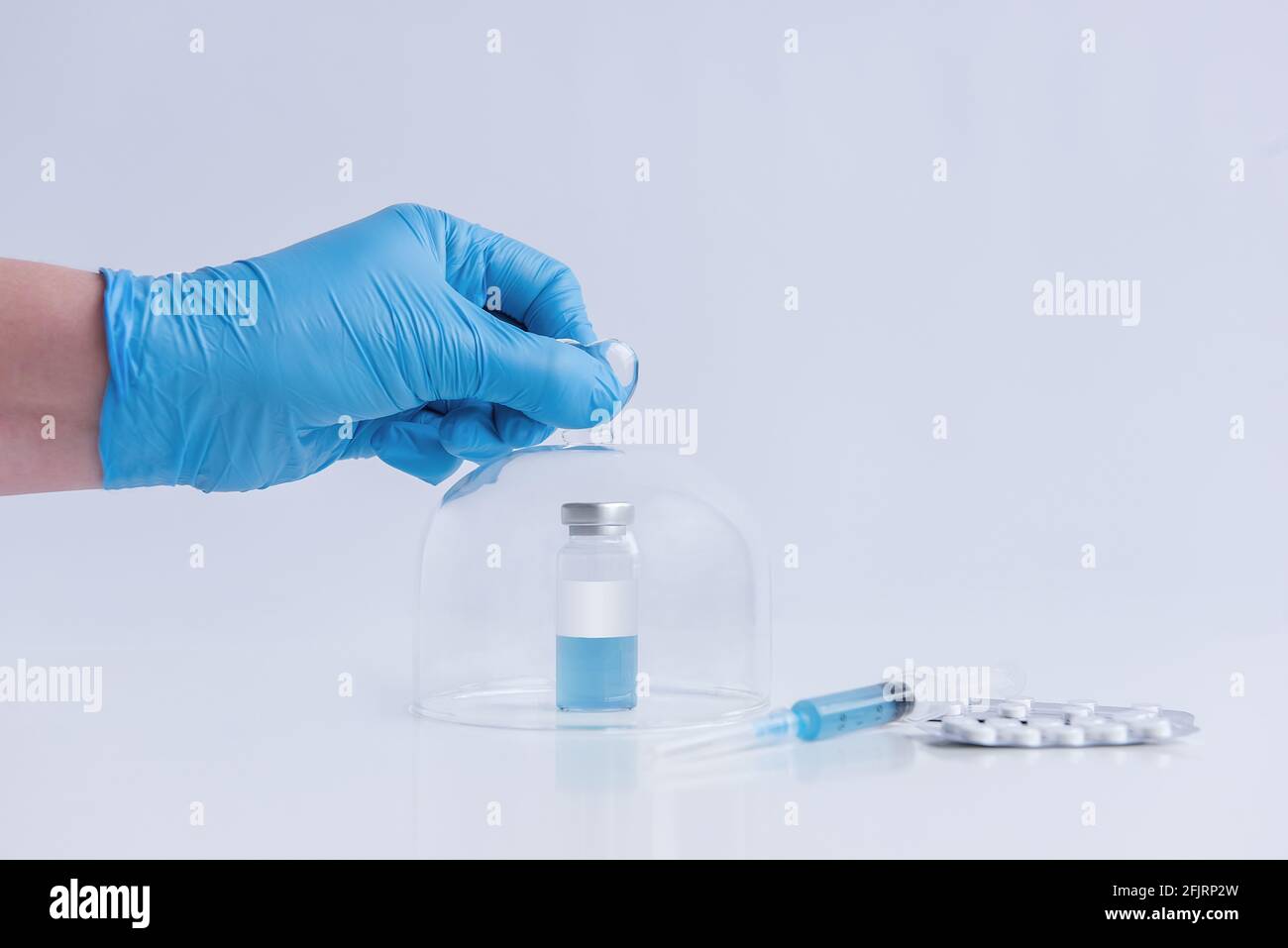 On a white isolated background stands the vaccine with a syringe, pills. The doctor's hand in a blue medical glove opens the programmed protective dom Stock Photo
