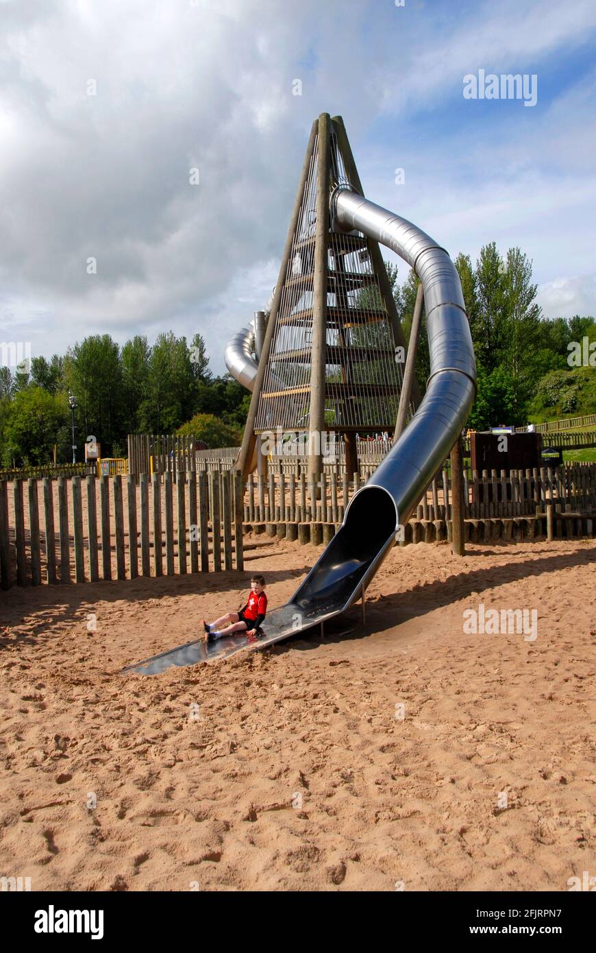 Tall four-sided structure with young boy in red emerging from curved enclosed tube acting as children's slide, Telford Town Park, Shropshire, England Stock Photo