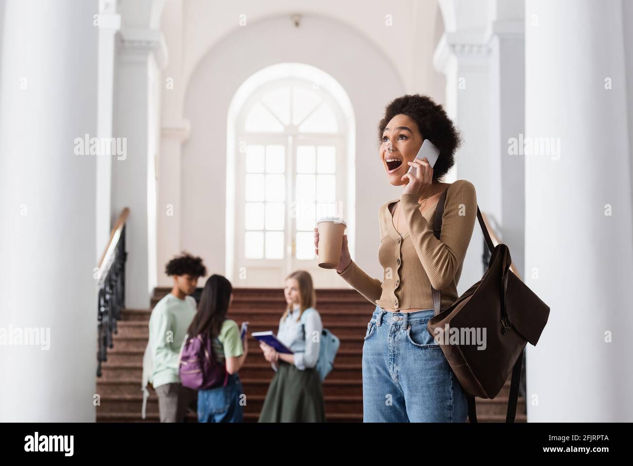 Excited african american student with coffee talking on cellphone Stock ...