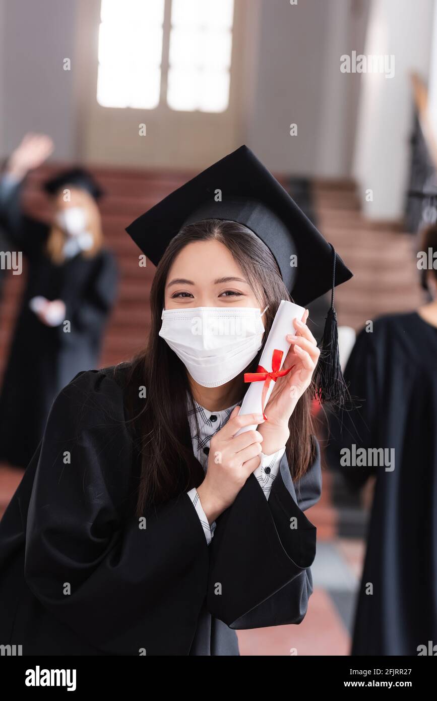 Asian graduate in academic dress and medical mask holding diploma with  ribbon Stock Photo - Alamy