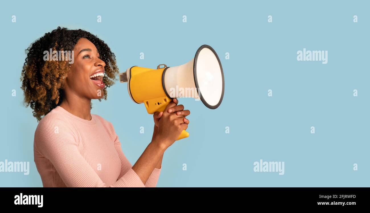 Announcement Concept. Cheerful Black Woman Shouting With Megaphone In Hands, Blue Background Stock Photo