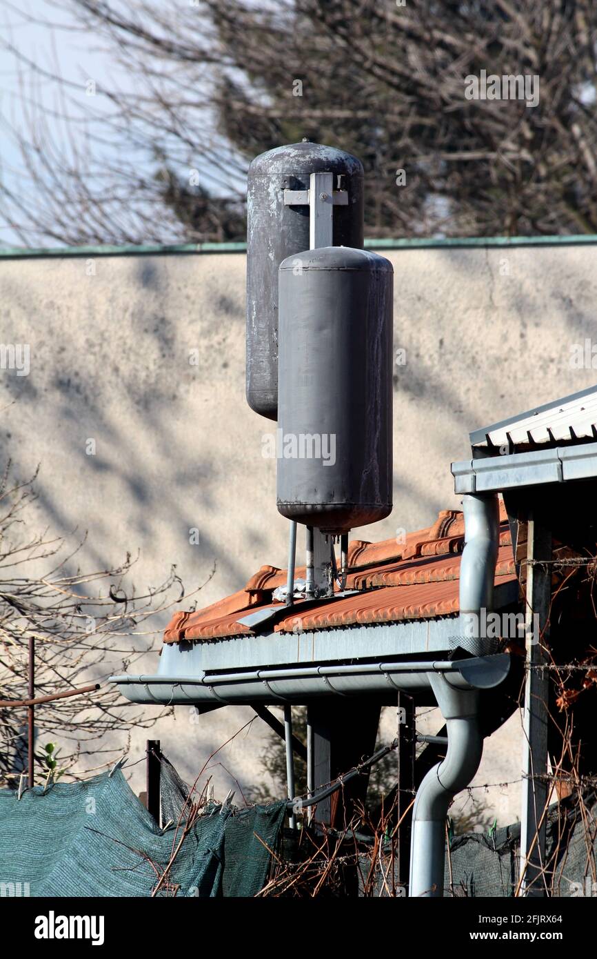 Two old heavily used water heater boilers painted black and converted into homemade solar water heaters mounted on top of family house roof Stock Photo