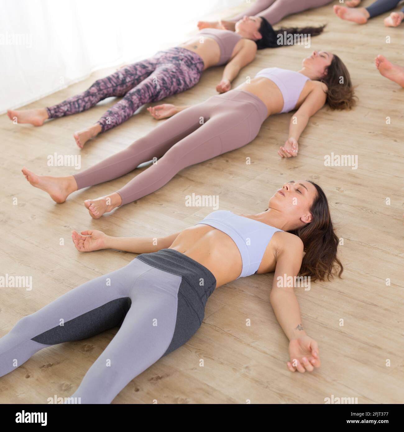 Group of young authentic sporty attractive people in yoga studio, practicing yoga lesson with instructor. Healthy active lifestyle, working out in gym Stock Photo