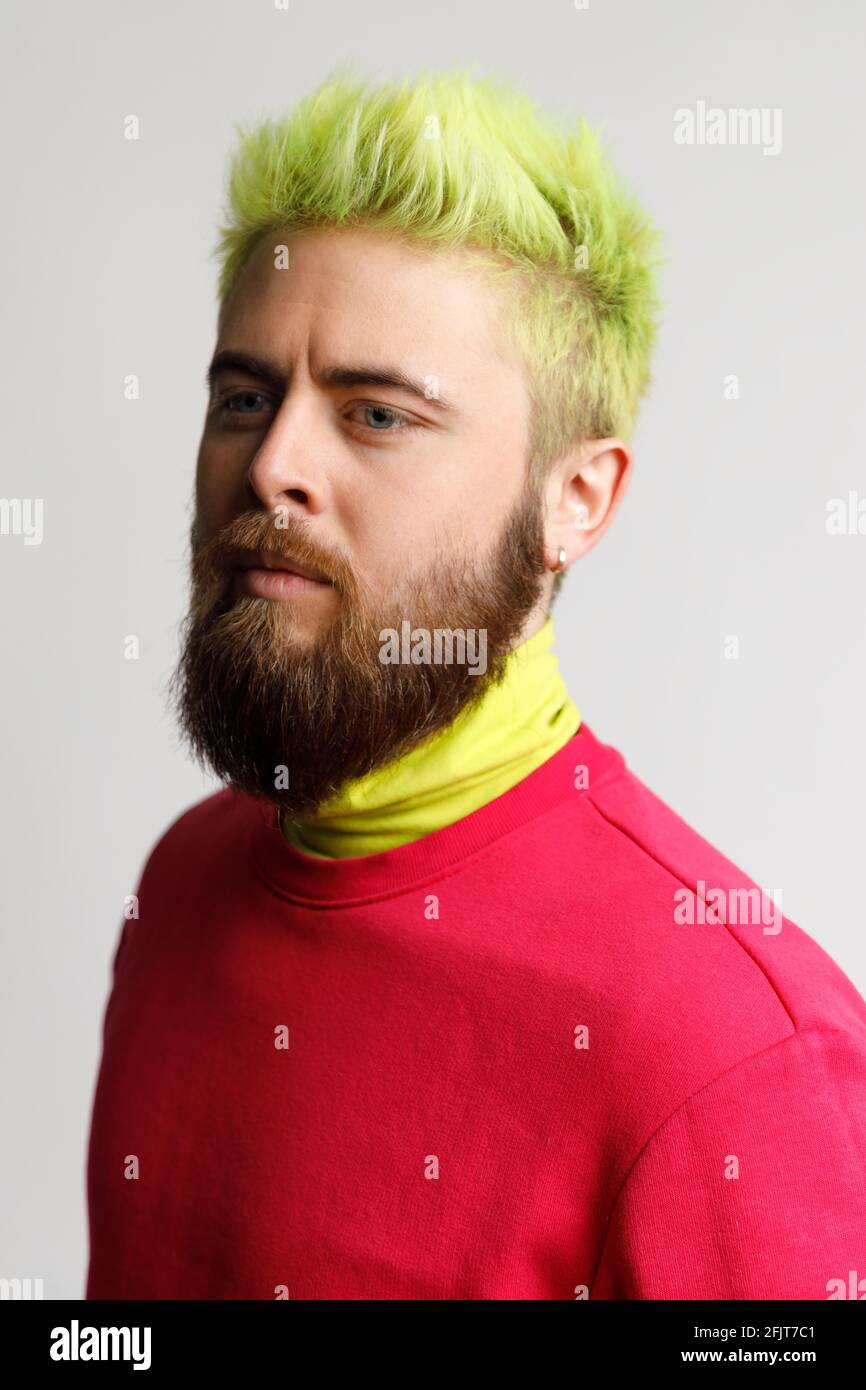 Portrait of serious handsome man with beard and yellow hair, wearing casual red jumper, looking focused at camera, has confident expression. Indoor st Stock Photo