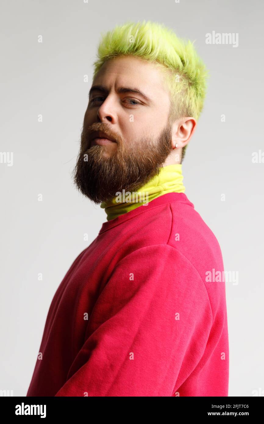 Portrait of proud handsome young bearded Caucasian man in red casual sweater, looking with prideful face,standing half sideways smug puffed. Indoor st Stock Photo