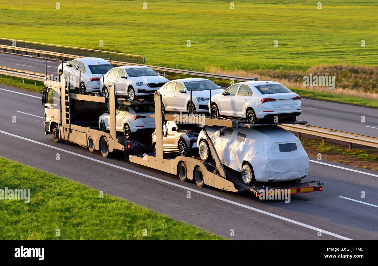 Car carrier trailer transports cars on highway on sunset background