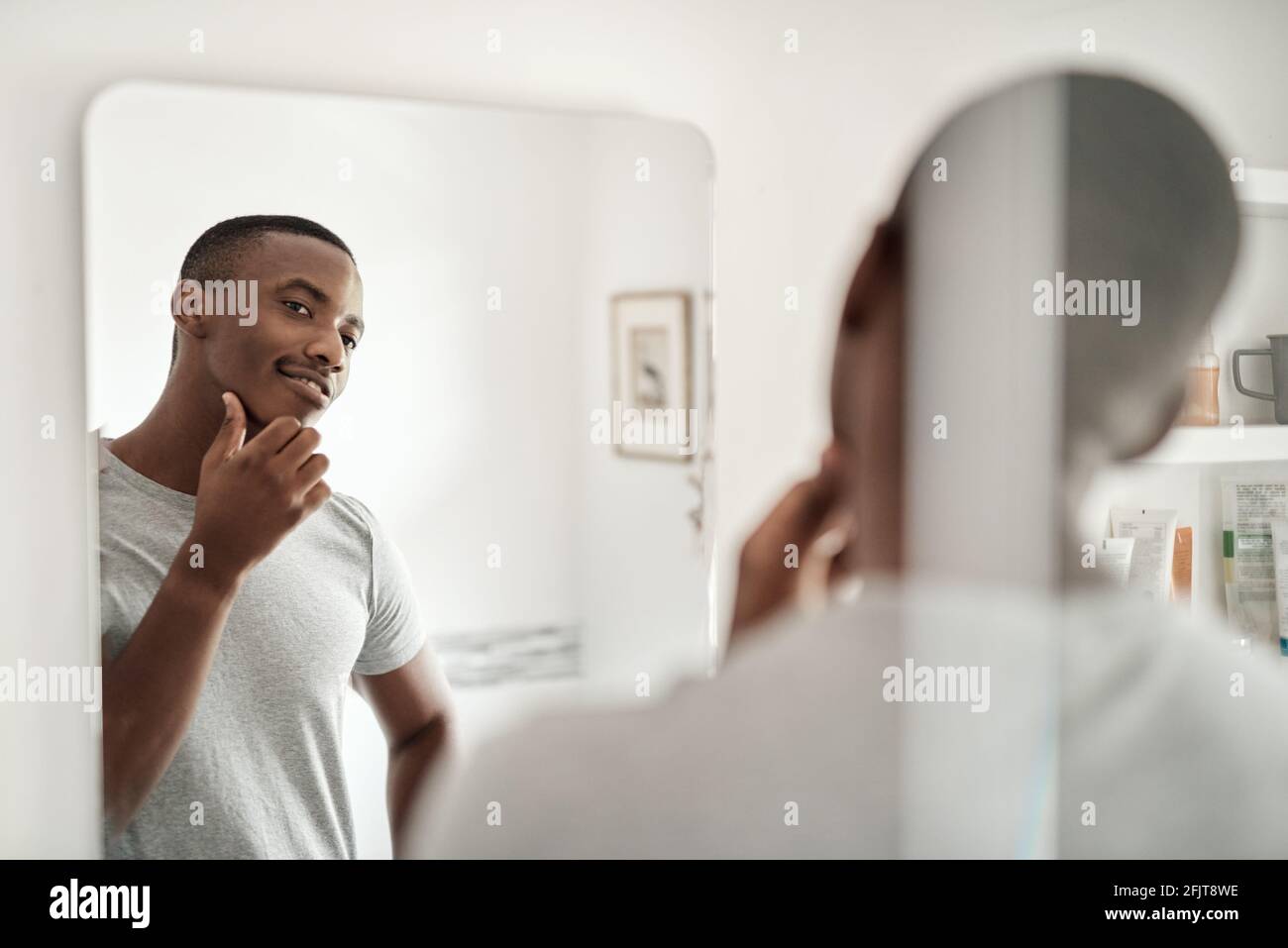 Smiling African man looking at his face in a bathroom mirror Stock Photo