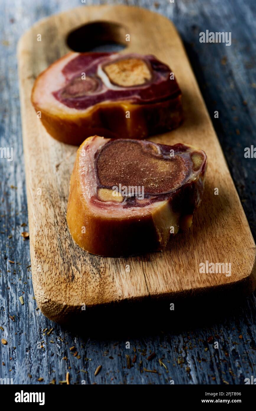 closeup of two cuts of codillo de jamon, spanish ham hock, on a chopping board placed on a gray rustic wooden table Stock Photo