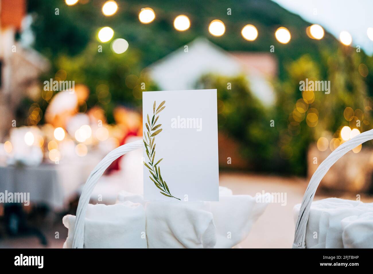 Blank card with ornament stands on rolled towel in white wicker basket on table Stock Photo