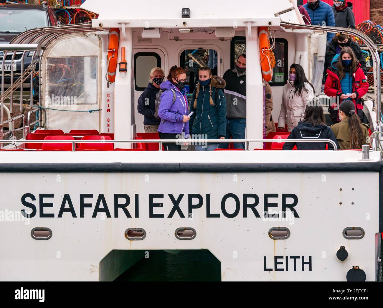 North Berwick, East Lothian, Scotland, United Kingdom, 26th April. Businesses reopen: with lockdown restrictions eased today, the Scottish Seabird Centre first tourist cruise boat outing takes place since last year. Pictured: Passengers board the Seafari Explorer catamaran wearing face masks Stock Photo