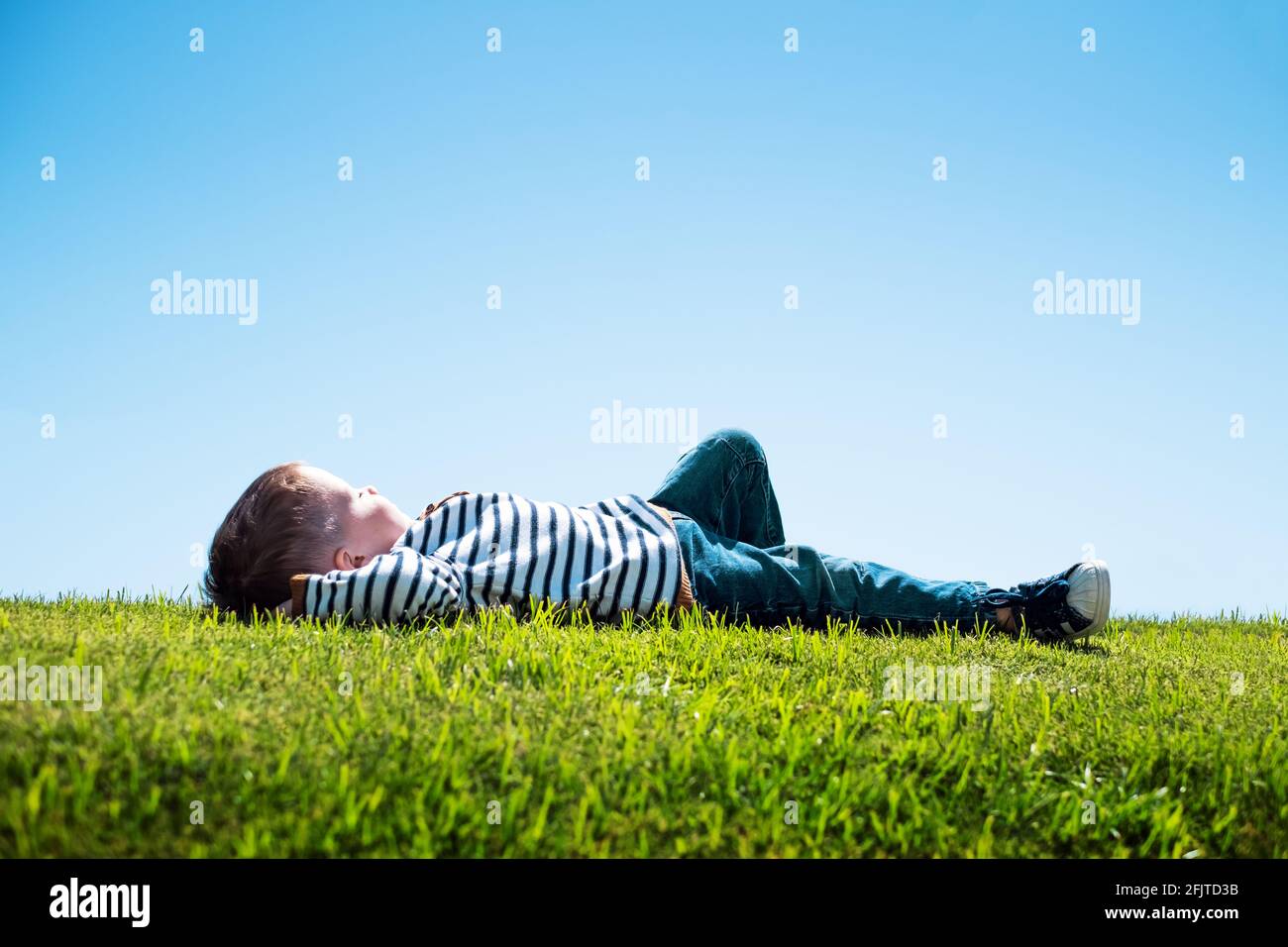 Happy little boy laying on green grass Stock Photo