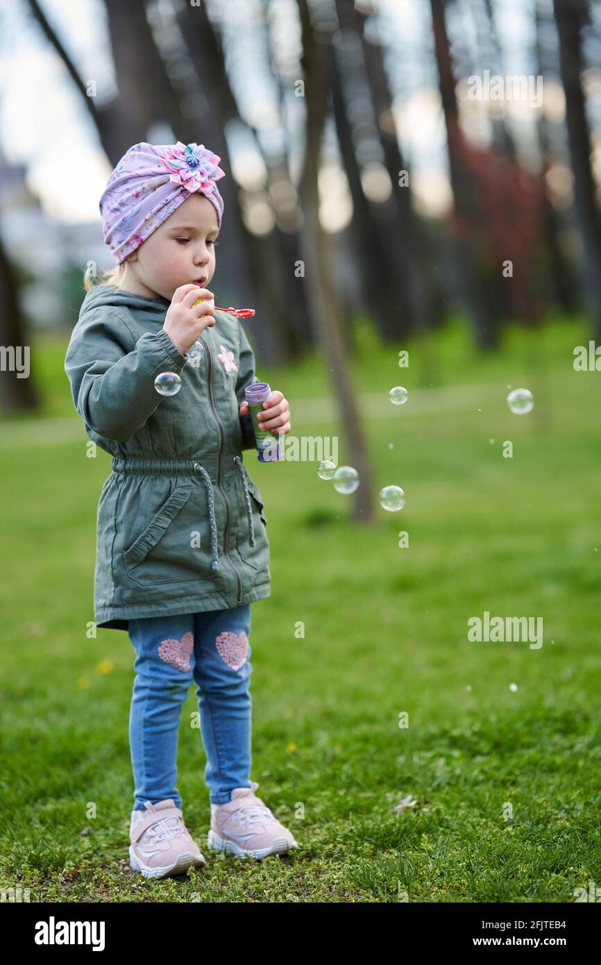 Happy little girl blowing soap bubbles in the park in a beautiful ...