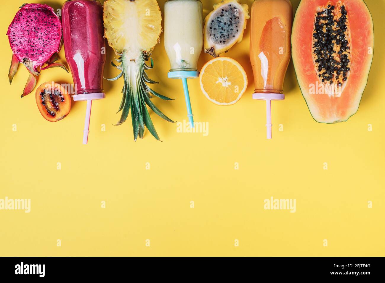 Fresh smoothie and juicy fruits - papaya, orange, pineapple, dragon fruit, pitahaya, tamarillo fruit over yellow background. Detox summer drink. Vegan Stock Photo