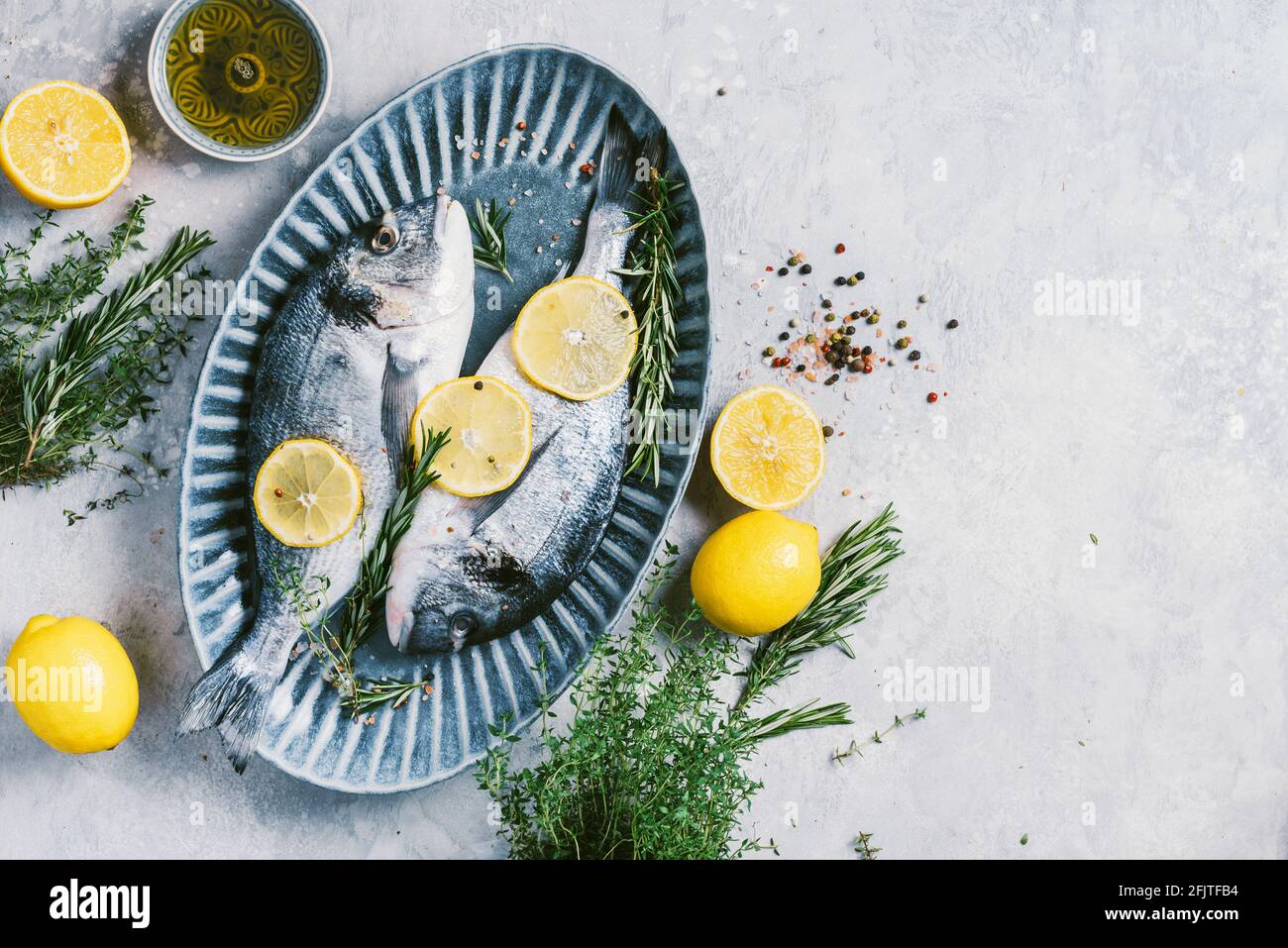 Fresh uncooked dorado or sea bream fish with lemon, herbs, oil, vegetables and spices on concrete background. Top view. Healthy food concept. Copy Stock Photo