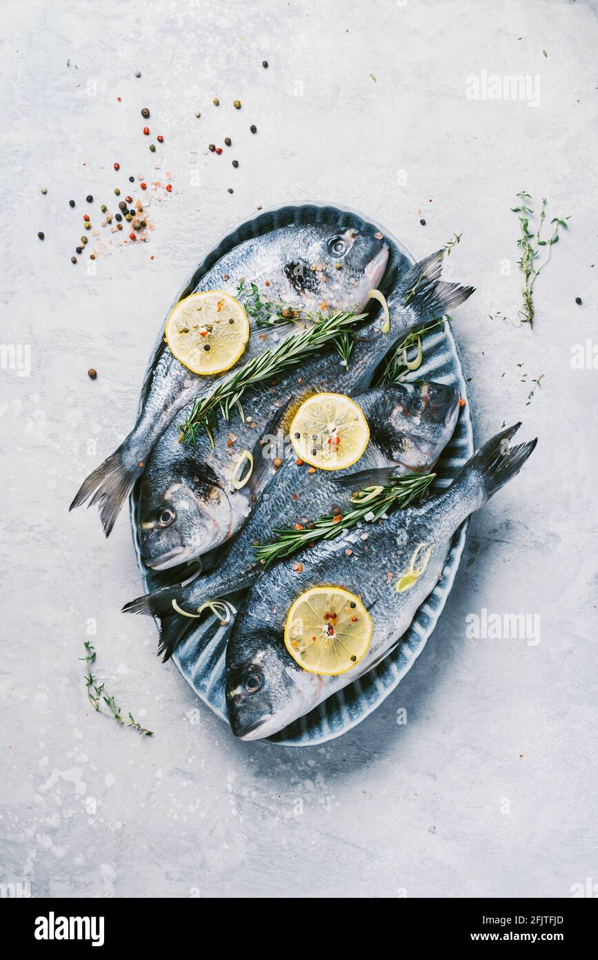 Uncooked dorado or sea bream fish with lemon, herbs, oil, vegetables and spices on concrete background. Top view. Healthy food concept. Copy space Stock Photo