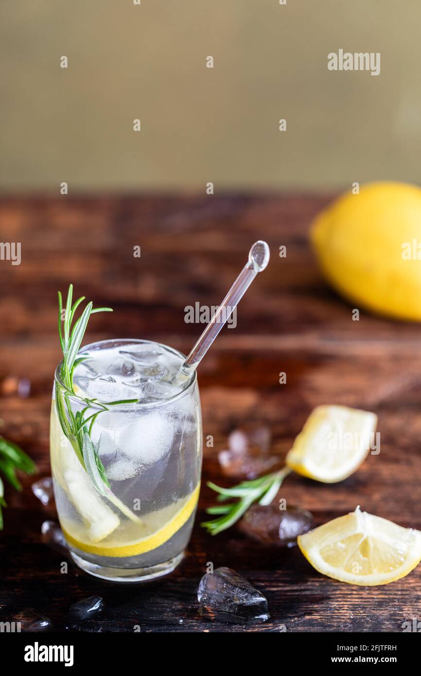 Lemon drink with rosemary and ice. Gin and tonic, GT. On a rustic wooden background. Refreshing cocktail or detox mocktail with homegrown herbs. Copy Stock Photo