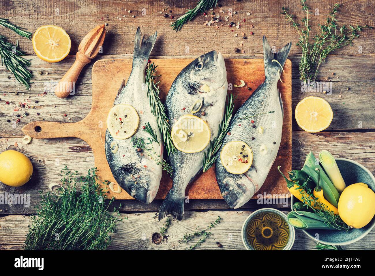 Raw dorado fish with ingredients, lemon, herbs, oil, vegetables and spices on wooden cutting board over wood background. Top view. Healthy food diet Stock Photo