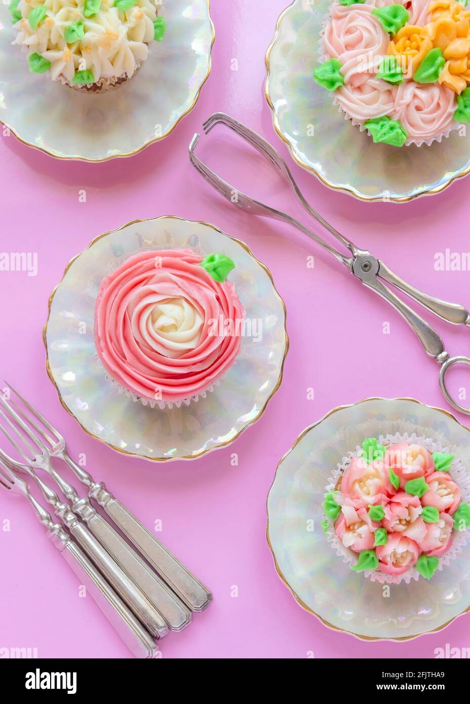 vertical overrview image of pretty delicately cup cakes iced with  Russian  piping icing tips ,pink background  and silverware with copy space Stock Photo