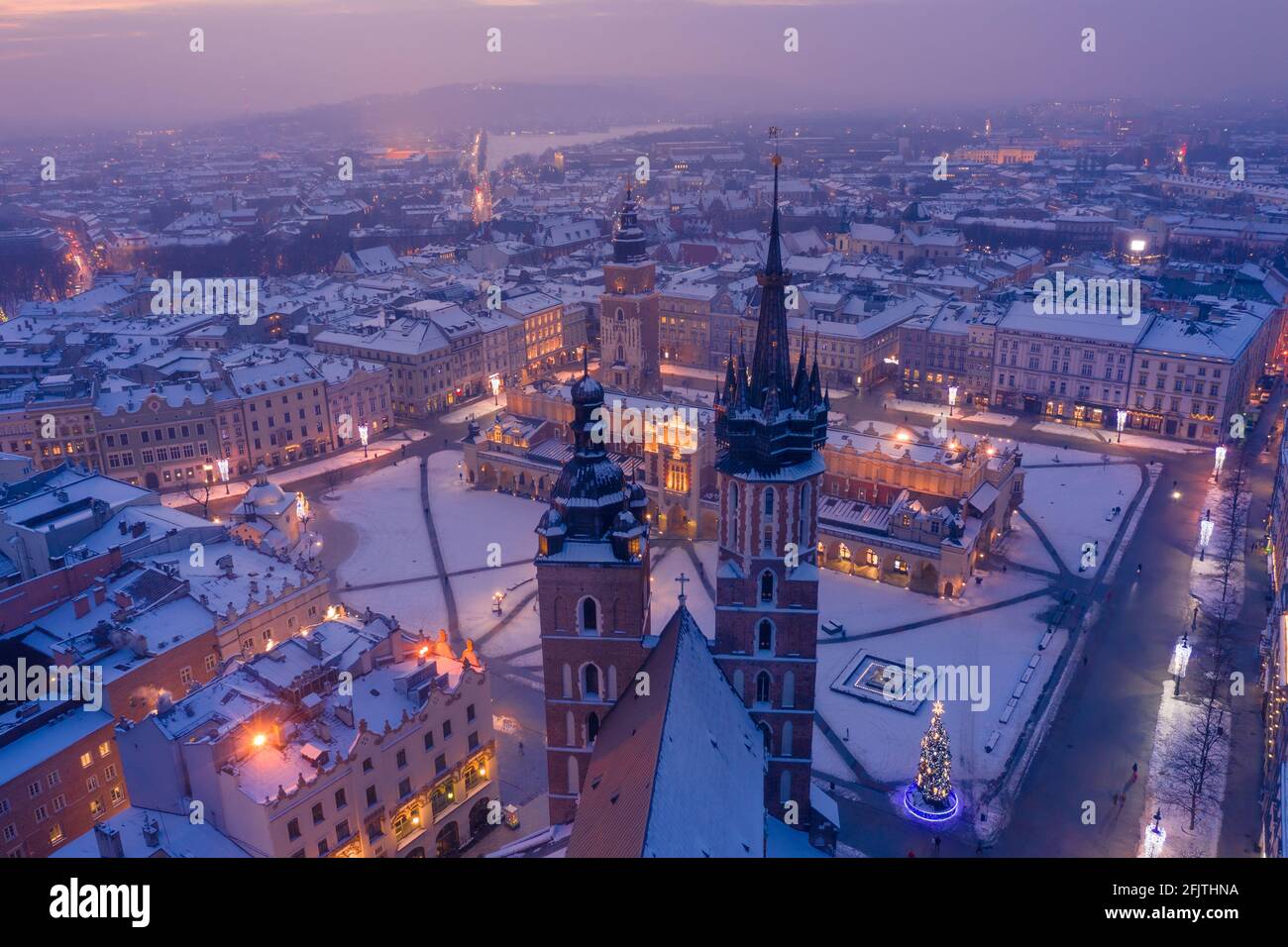 Main square Rynek of the Old Town of Krakow Poland in winter. St. Mary's Basilica Gothic church and Krakow Cloth Hall, covered in snow at evening with Stock Photo