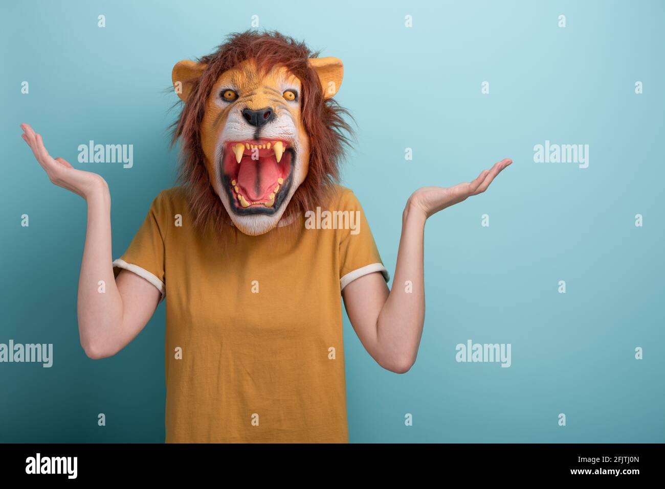 Confused young woman in lion mask standing and shrugging shoulders Stock Photo