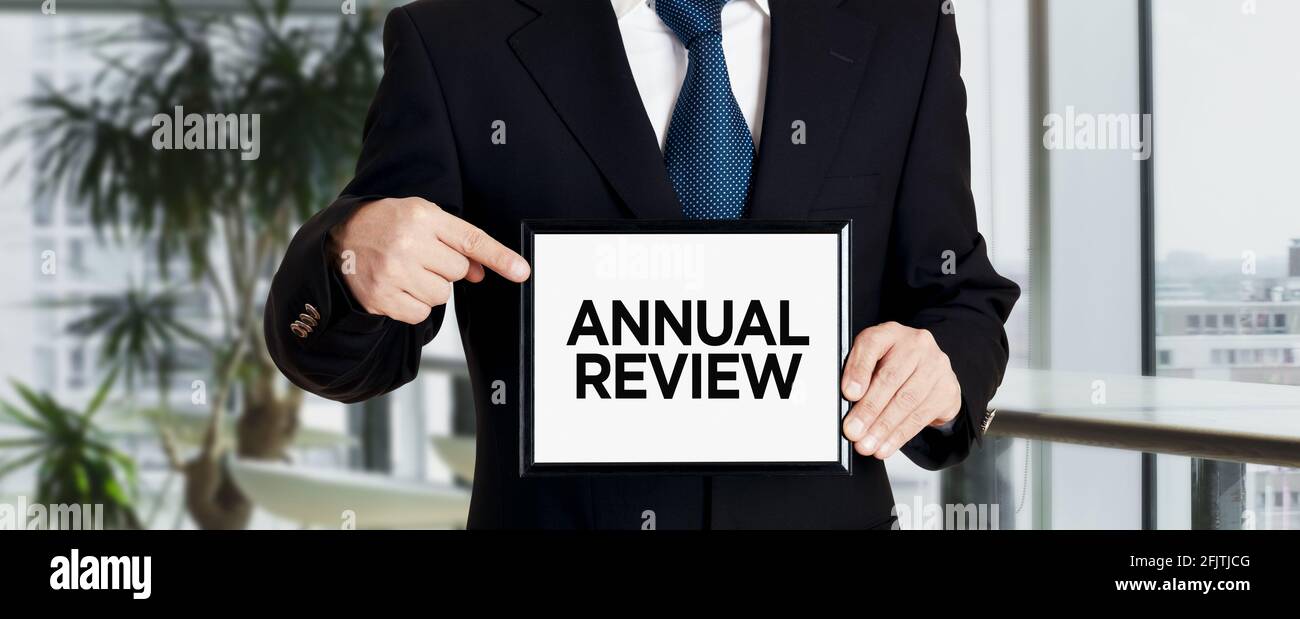Businessman holds a signboard and points his finger to the message annual review. Annual business evaluation concept. Stock Photo