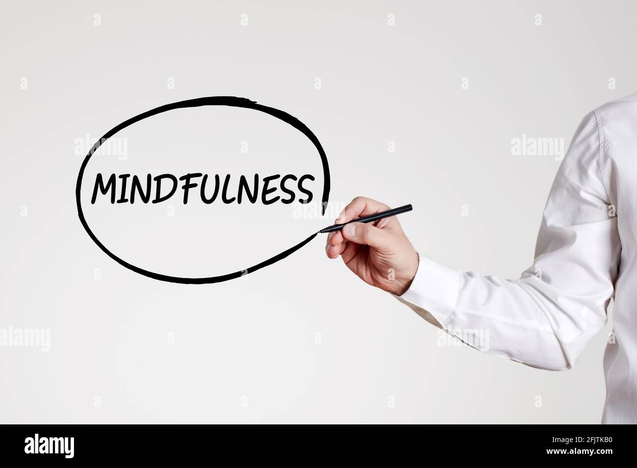 Businessman writes the word mindfulness with an outline circle on gray background. Relaxation and stress free work environment concept. Stock Photo