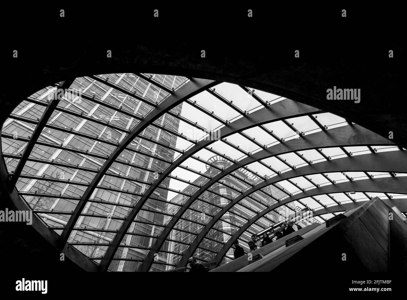 The curved glass canopy over the entrance of Canary Wharf underground / tube station, London, UK seen from inside / below. B&W Stock Photo