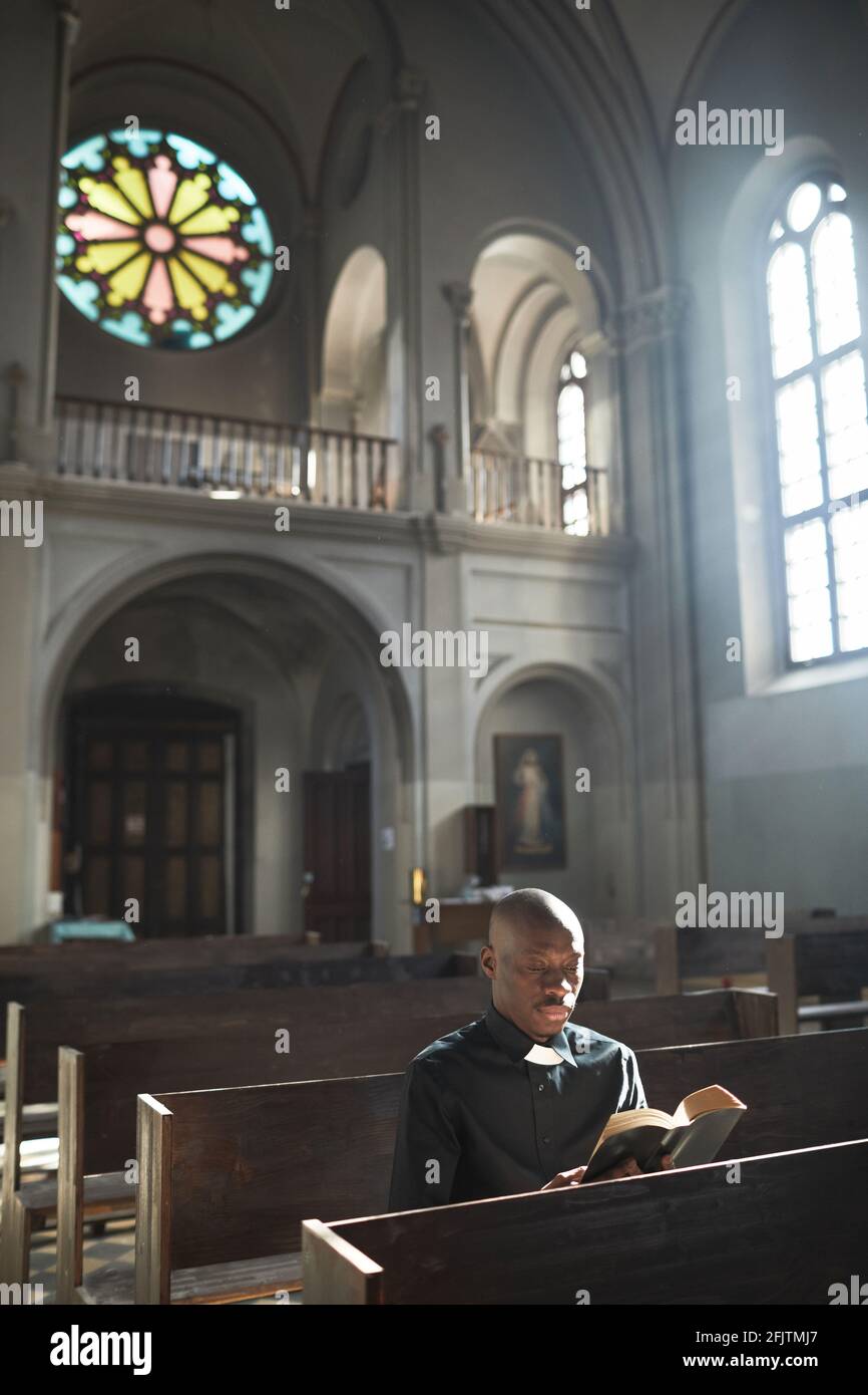 African priest sitting on the bench in church reading the Bible and praying Stock Photo