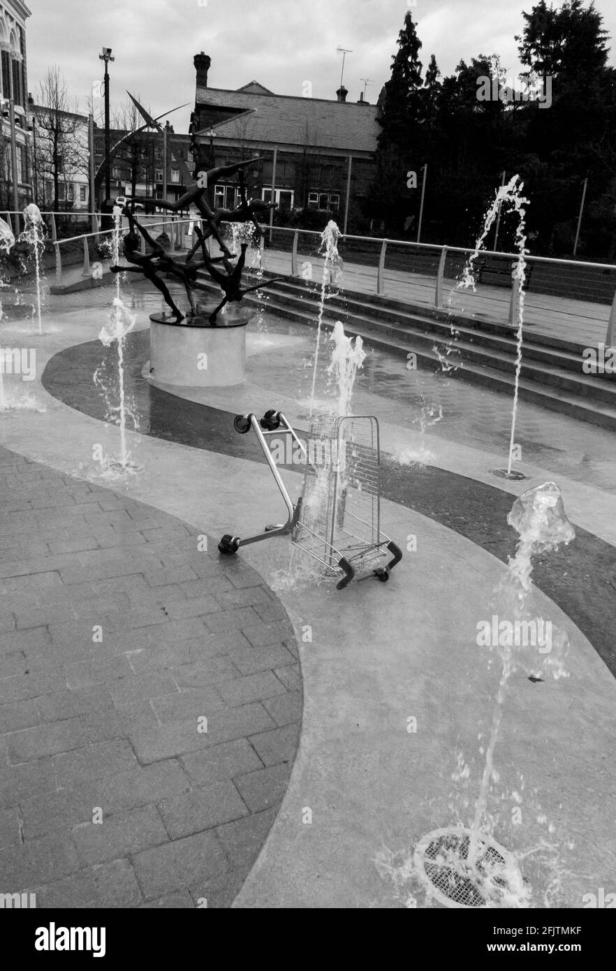 A shopping trolley dumped in the water fountain by the The Five Swimmers (a sculpture by David Wynne) in front of Staines Town Hall, UK. B&W. Stock Photo