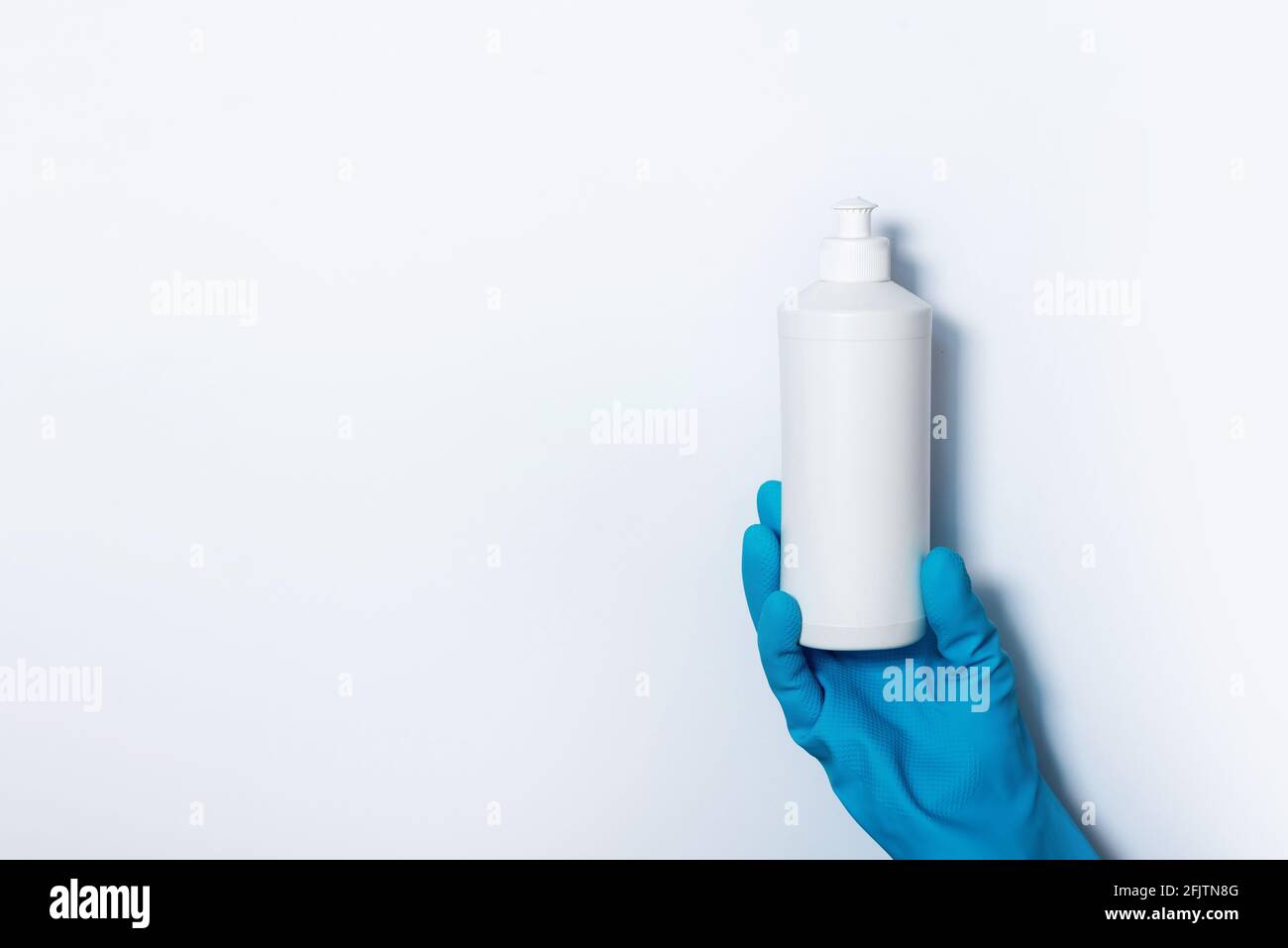 Hand in glove holding white plastic bottle of cleaning product, household chemicals. Copy space. Cleaning service concept. Household chemical cleaning Stock Photo