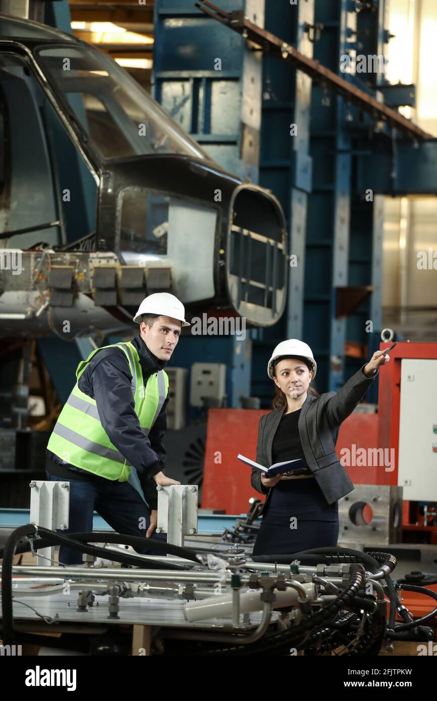 Portrait of a female factory manager in a white hard hat and business suit and factory engineer in work clothes. Controlling the work process at the airplane manufacturer. Stock Photo