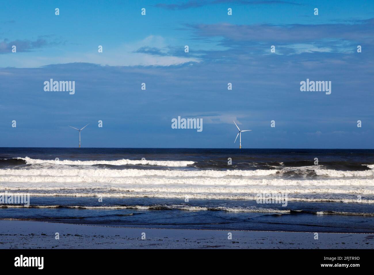 Turbines at Blyth Offshore Windfarm in Northumberland, England. North Sea waves roll into the beach at Blyth. Stock Photo