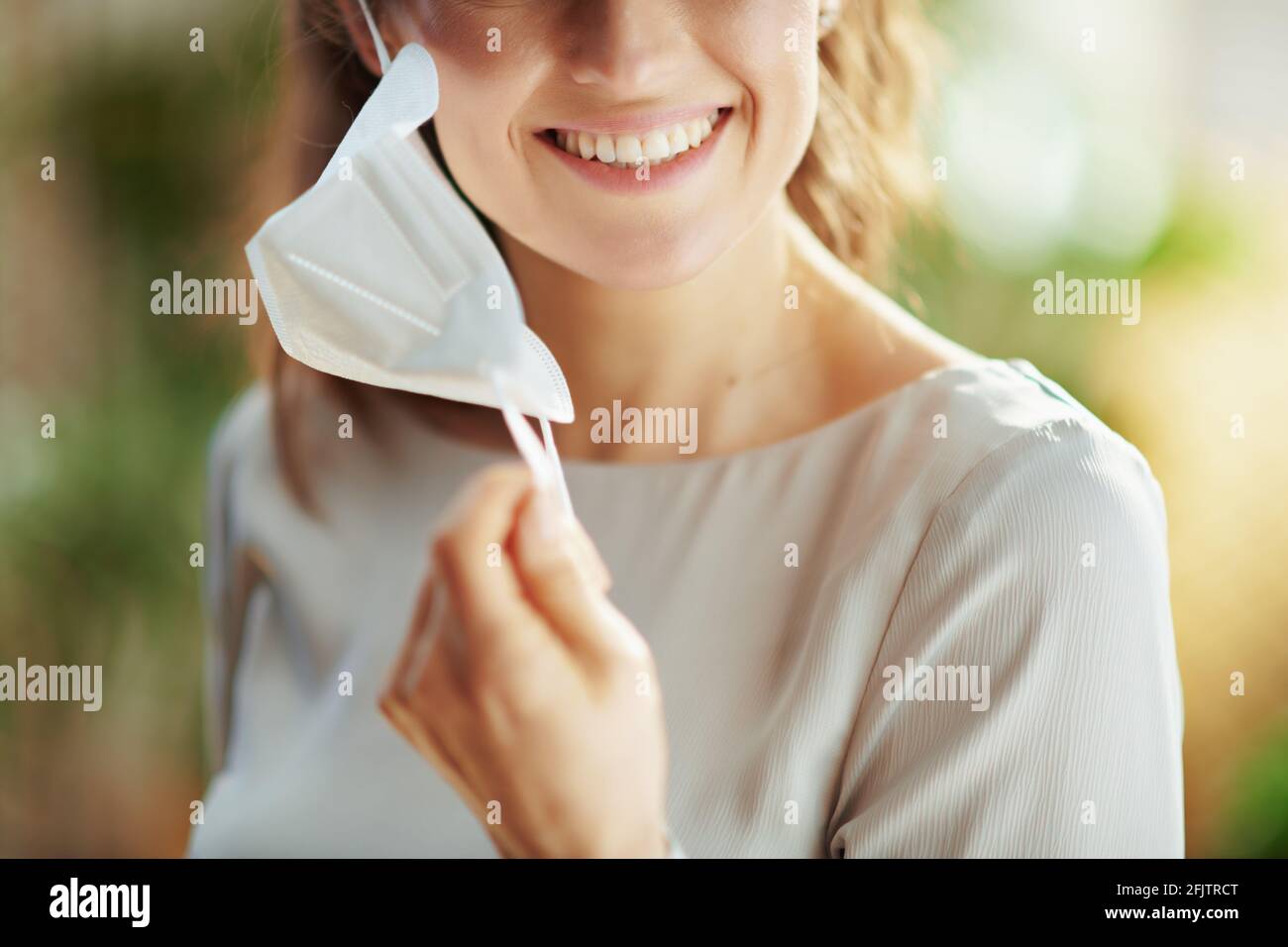 covid-19 pandemic. Closeup on smiling female in grey blouse taking off ffp2 mask. Stock Photo
