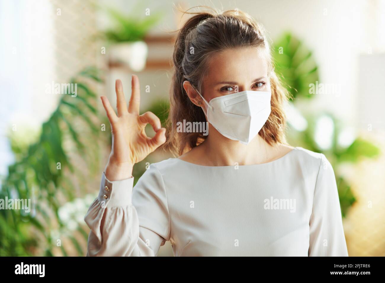 coronavirus pandemic. happy young woman in grey blouse with ffp2 mask showing ok gesture. Stock Photo