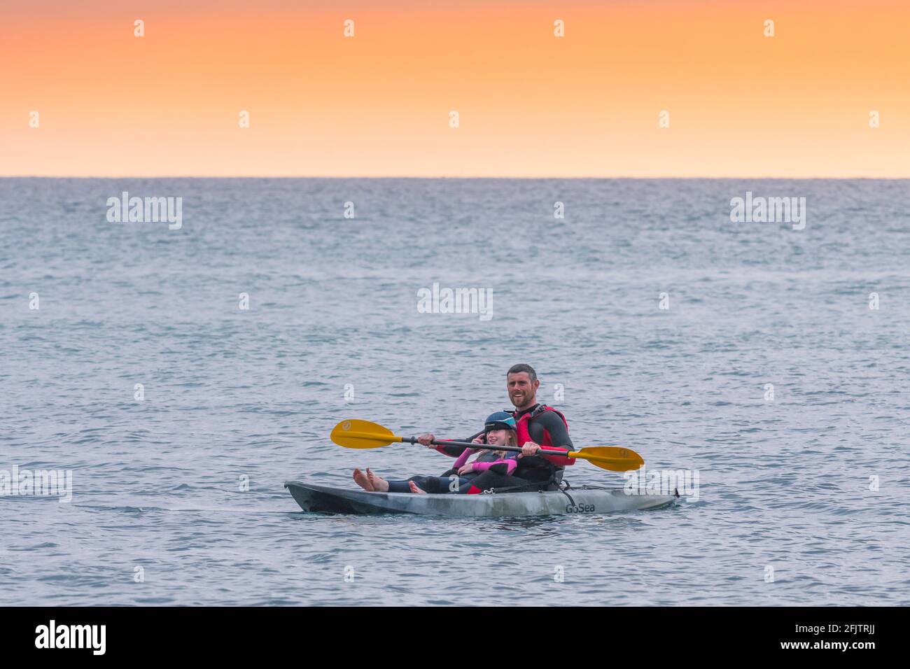 A holidaymaker and his young daughter on a GoSea Sit-on-Top kayak in the sea in evening light at Little Fistral in Newquay in Cornwall. Stock Photo
