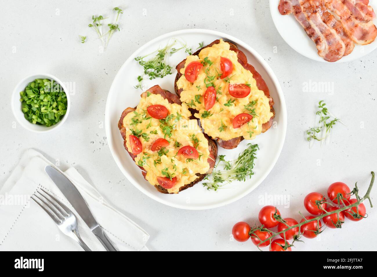 Scrambled eggs with microgreen, bacon and tomatoes on bread. Top view, flat lay Stock Photo