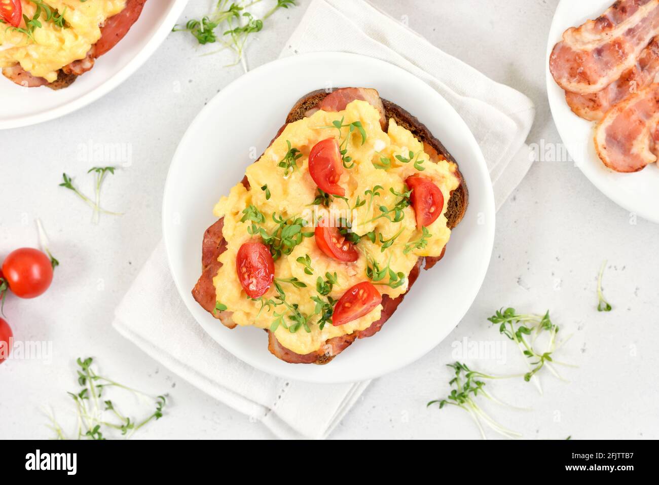 Scrambled eggs with microgreen, bacon and tomatoes on bread. Top view, flat lay Stock Photo