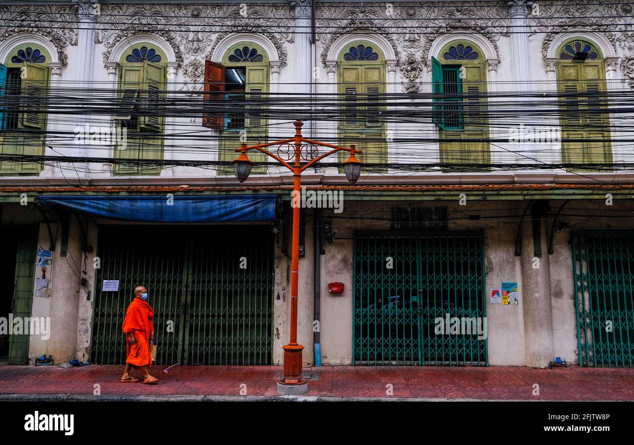 A Thai monk walks past a colorful old building in Bangkok, Thailand Stock Photo