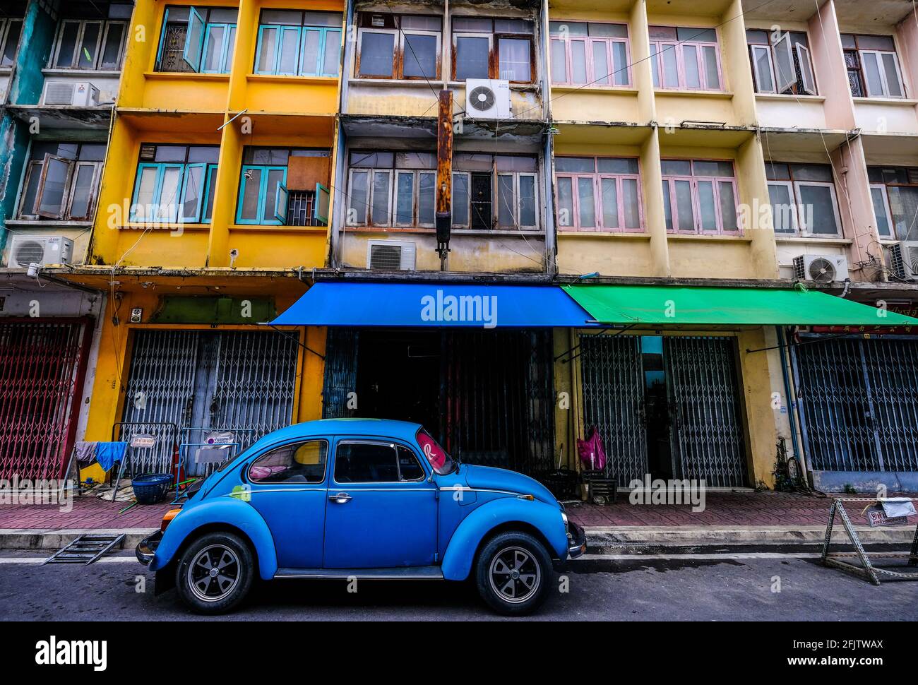 An old blue VW Beetle is parked in the street in front of a row of colorful buildings in the Chinatown area of Bangkok, Thailand Stock Photo