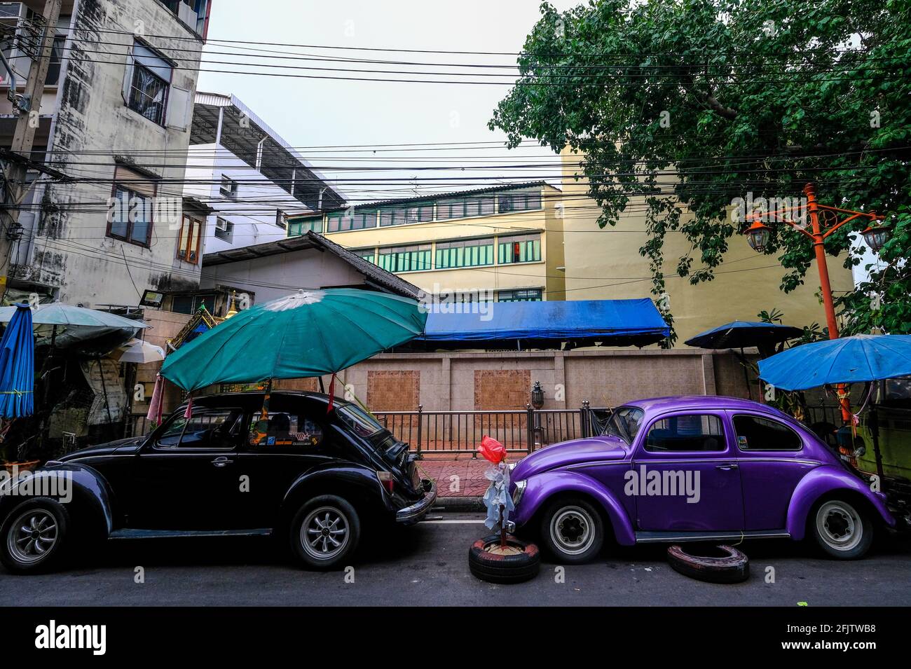 Two old VW Beetle cars are parked in a street in the Chinatown area of Bangkok, Thailand Stock Photo