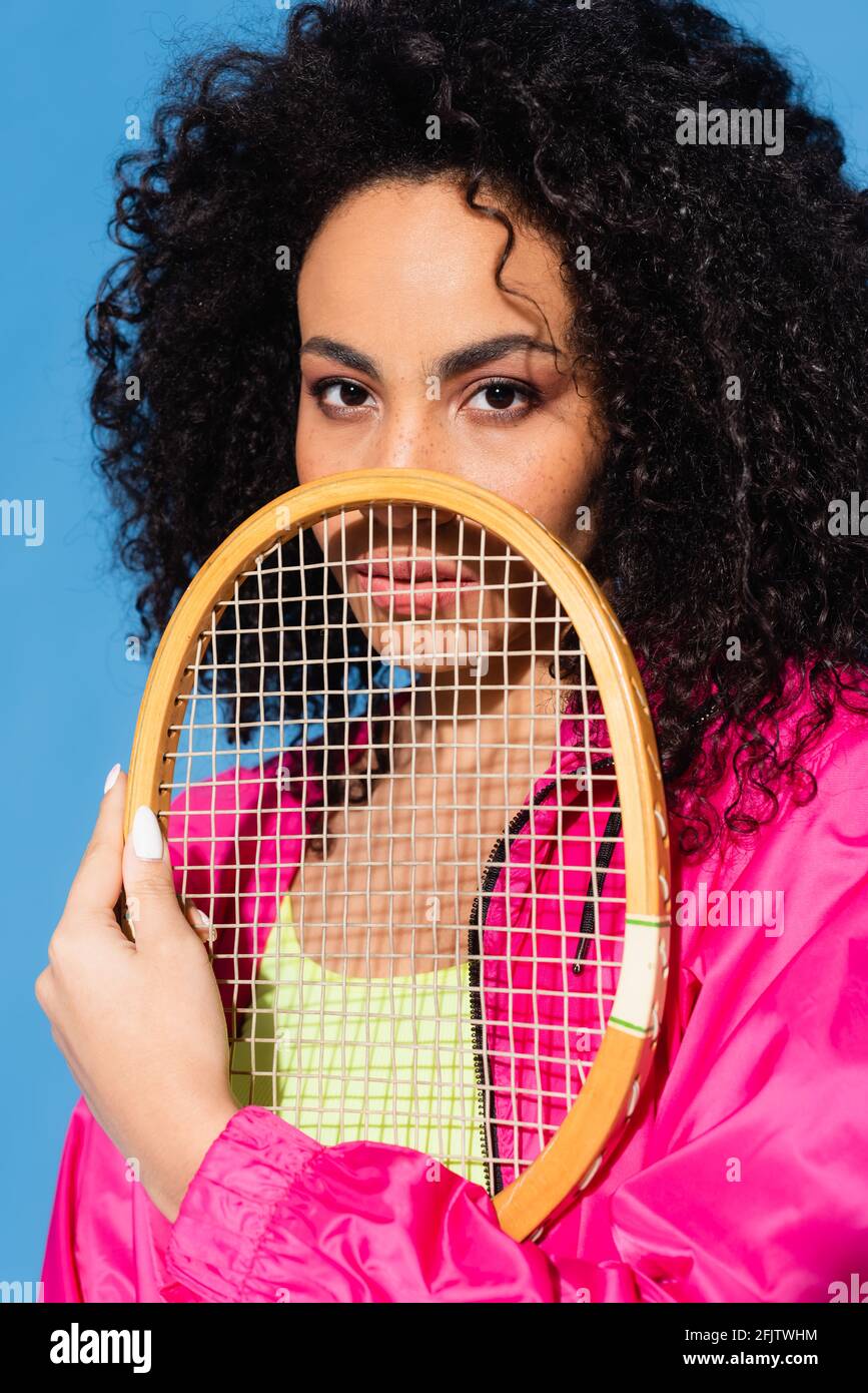 curly african american woman posing with tennis racket while looking at ...