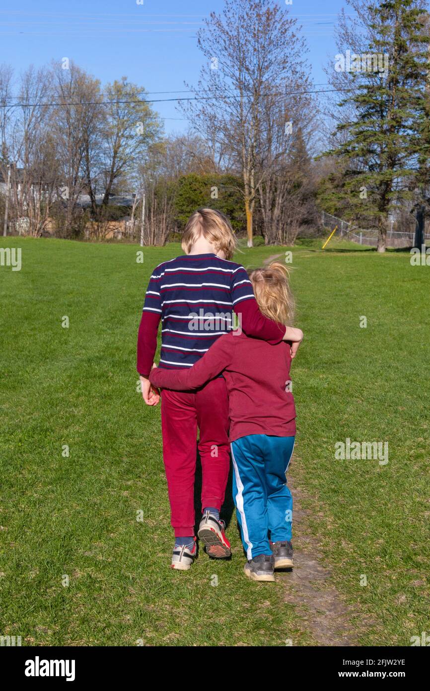 Children walking in the park in spring. Siblings hugging. Family and friendship concept. Brother and sister together from behind. Candid moment. Stock Photo