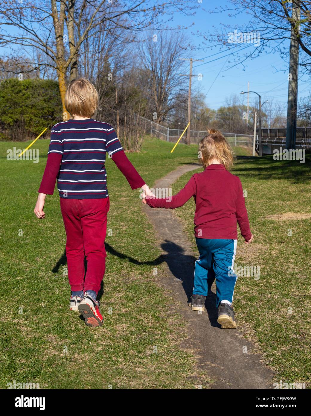 Children walking in the park in spring. Siblings holding hands. Family and friendship concept. Brother and sister together from behind. Stock Photo
